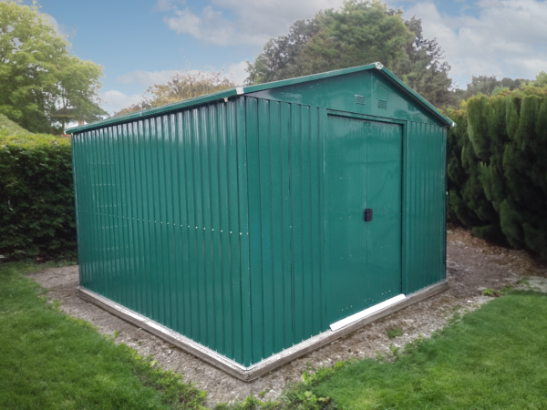 The 10ft x 10ft steel garden shed from Sheds Direct Ireland. It is a green, steel shed with vertical panels. The doors are closed, there is a metal frame around the edge at the bottom and there is grass in the foreground of the scene and blue skies above the shed
