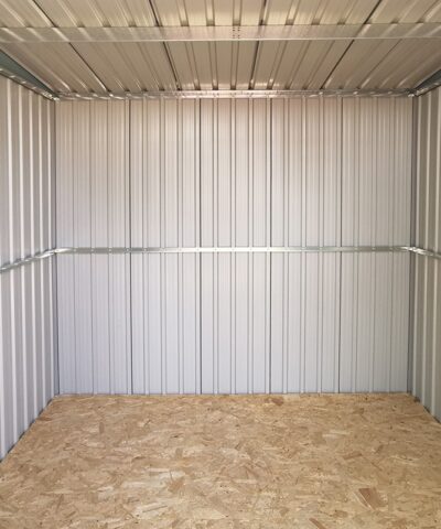 A view of the inside of the steel pent shed. The floor is a brown ply and the walls are a pale grey with a brace running across them.