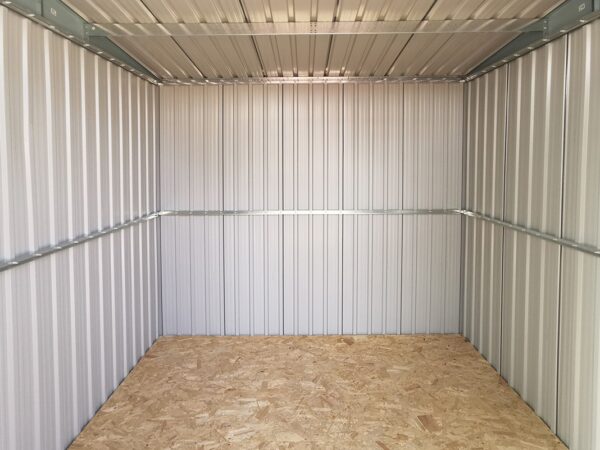 A view of the inside of the steel pent shed. The floor is a brown ply and the walls are a pale grey with a brace running across them.