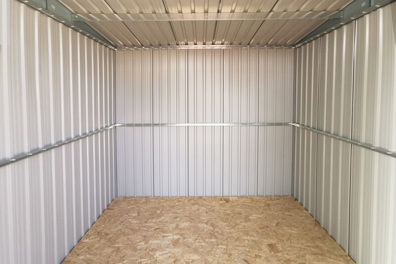 A view of the inside of the steel pent shed. The floor is a brown ply and the walls are a pale grey with a brace running across them.