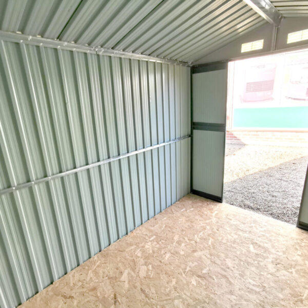 An internal wide angled view of the 6x9 steel shed. It's taken from the corner and the door is visible. The walls are grey, there is green trimmings around the door. The floor is plywood.