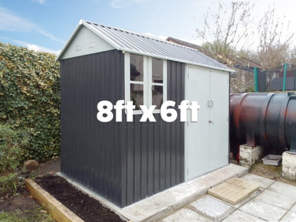 The 8ft x 6ft Steel Cottage shed on a solid, paving slab base. Behind it there is large black tubing and to the other side there is a large, tall hedgerow