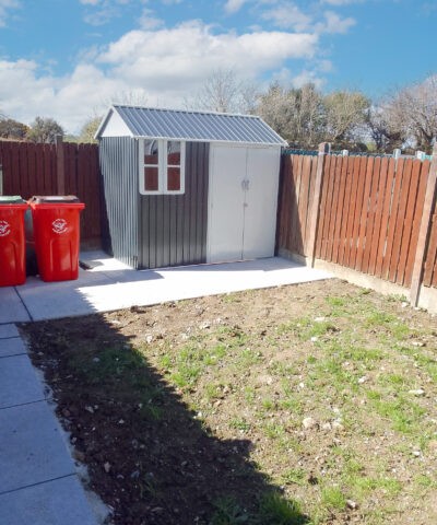 the cottage shed in a long garden, with red wheelie bins beside it