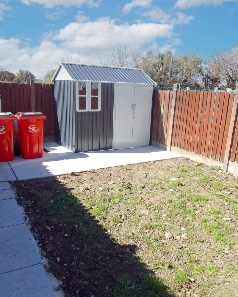the cottage shed in a long garden, with red wheelie bins beside it