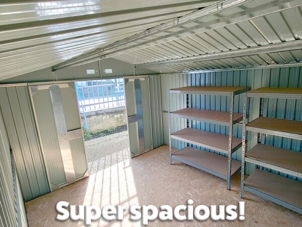 Inside the Colossus shed with the text 'SUPER SPACIOUS!' written in white text along the bottom. The shed is a silvery colour inside with light coming in the door and streaking across the floor. There are two large shelving units inside this shed.