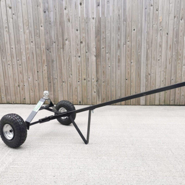 A black trailer dolly with silver, circular ball attachment. The trailer dolly is in a flat position with the handle pointing upwards at a 30 degree angle. It's sitting on a pale paving slab with a wooden wall behind it.