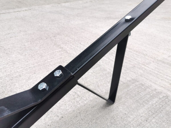 a detailed view of the triangular stand which is connected to the handle. This allows the trailer dolly to stand upright when not in use. The handle is connected to the wheels and axel and because of this bar, it raises at a 30 degree angle