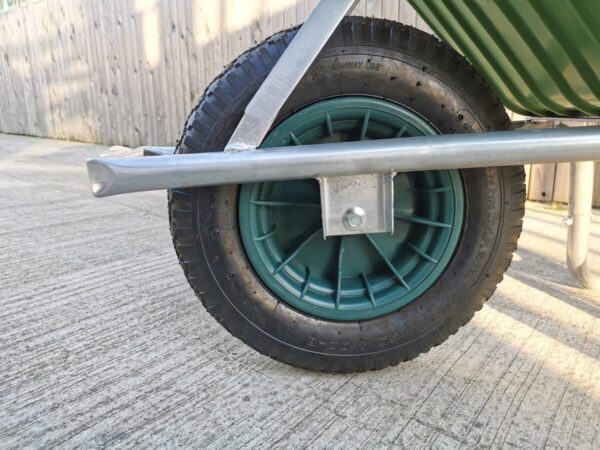 The view of the single wheel on the 90L wheelbarrow from Sheds Direct Ireland. The tyre is black, with a dark green inlat and the square wheel protector is flat to facilitate tipping