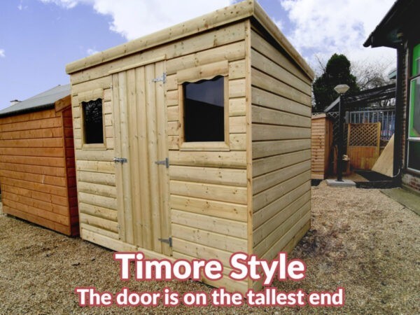 A timore style wooden cabin. It's seen from the right. The front and left side fo the shed are visible, the door is on the front and the roof slopes from the front to the back. There are two scalloped windows visible too
