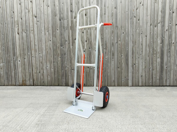 The aluminium hand truck with fold down footplate against a wooden wall