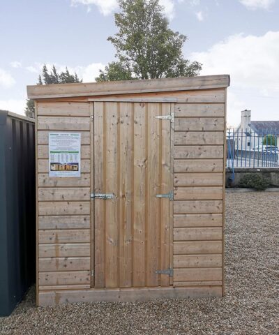 A cabin shed in the sheds direct Ireland showroom. It has a sloped room, a door which is not at ground level (there is a step up to it) and the wood pattern is horizontal. It is a pale wood and the steel hinges and lock are easily visible on it.