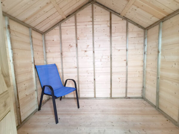 Interior view of the chalet shed as seen from the door. There is a blue deck chair on the left side of the image. The walls and floor are made of a pale golden-pink wood. The frae edges are a darker colour and some have printed numbers on them in a very faded black ink.