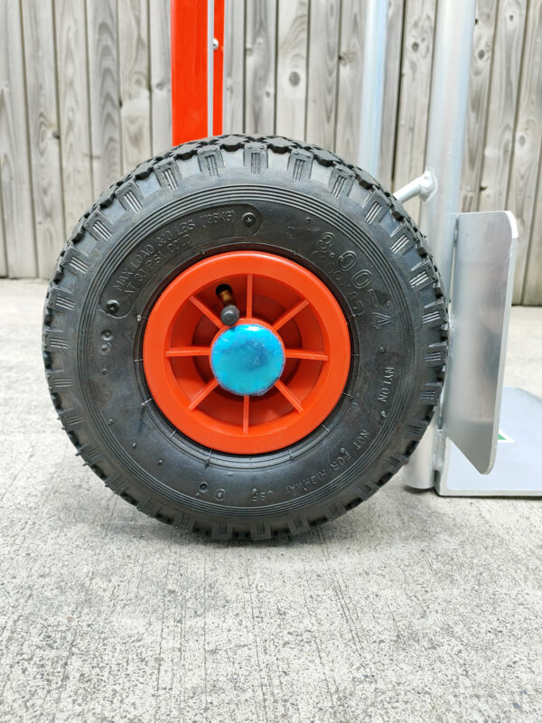 A profile view of the tyre on the aluminium sac truck. The tyre is a soft rubber looking piece, with a red circle in the centre with a metallic blue cap on the centre.