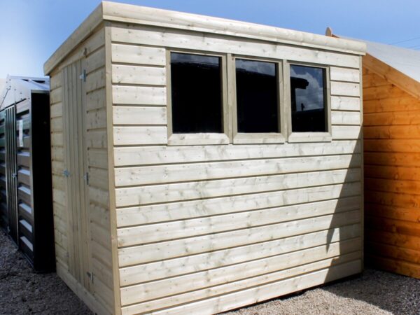 A Wooden Cabin Shed which has been Pressure Treated. The wood is slightly faded in colour because of the pressure treatment. There are three windows on the side of the shed and the door is on a different side to these windows.