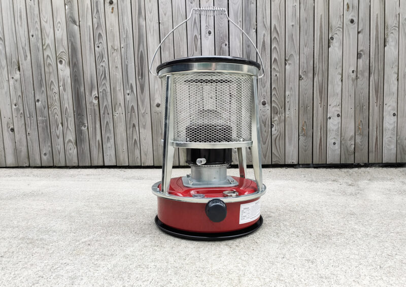 A red camping stove against a wooden wall.