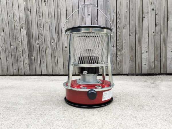 A red camping stove against a wooden wall.