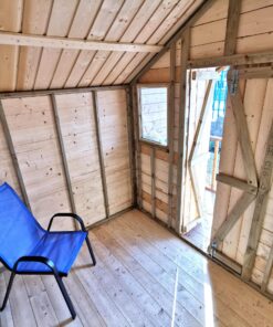 A view of the inside the wooden chalet shed. The shed is a pale brown colour with darker support beams. There is a blue chair in the middle of the shed.