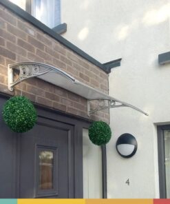 A customers photos showing a door canopy installed above a greay door onto some redbrick. There are two circular flower beds suspended from the door canopy and above the canopy there is a clear blue sky.