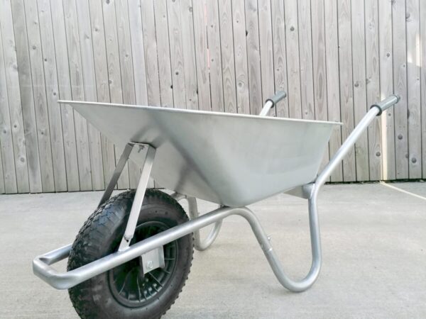 A steel wheelbarrow standing upright against a wooden fence
