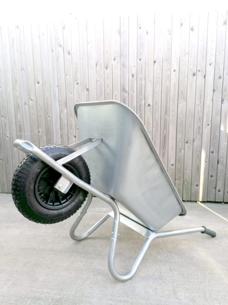 The steel wheelbarrow is lying on its back, the handles and support bars are on the ground and the wheel is raised. It takes up less floor space like this.