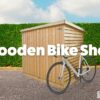 The Wooden Bike Shed seen from the right hand side. big bold text that reads wooden bike shed. a white bike leans onto shed