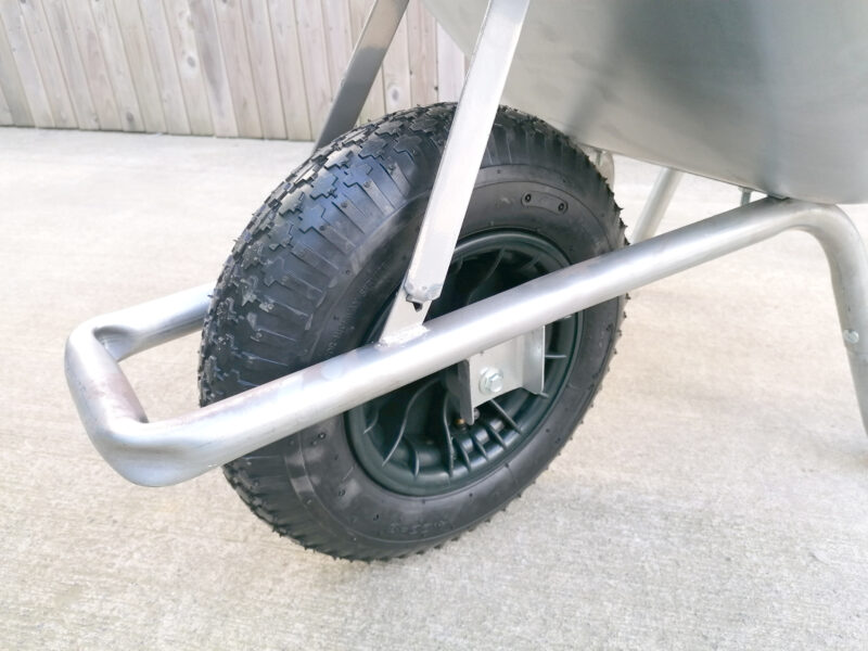 A close, cropped shot of the tyre on tthe steel wheelbarrow. It is a large, black inflatable tyre with deep inlay grooves for traction.