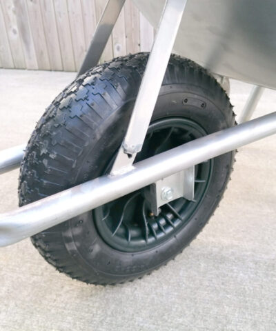 A close, cropped shot of the tyre on tthe steel wheelbarrow. It is a large, black inflatable tyre with deep inlay grooves for traction.