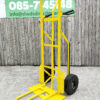 The side view of the bright yellow industrial hand truck. It's against a wooden wall and the extendable base plate has been folded out