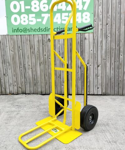 The side view of the bright yellow industrial hand truck. It's against a wooden wall and the extendable base plate has been folded out