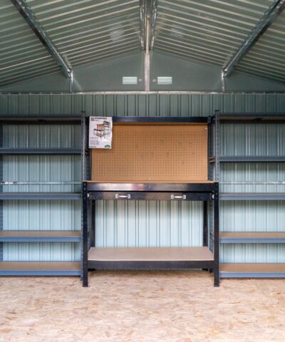 Shelves inside steel shed beside a metal work bench. There are 5 tiers and the tiers have wooden bases.