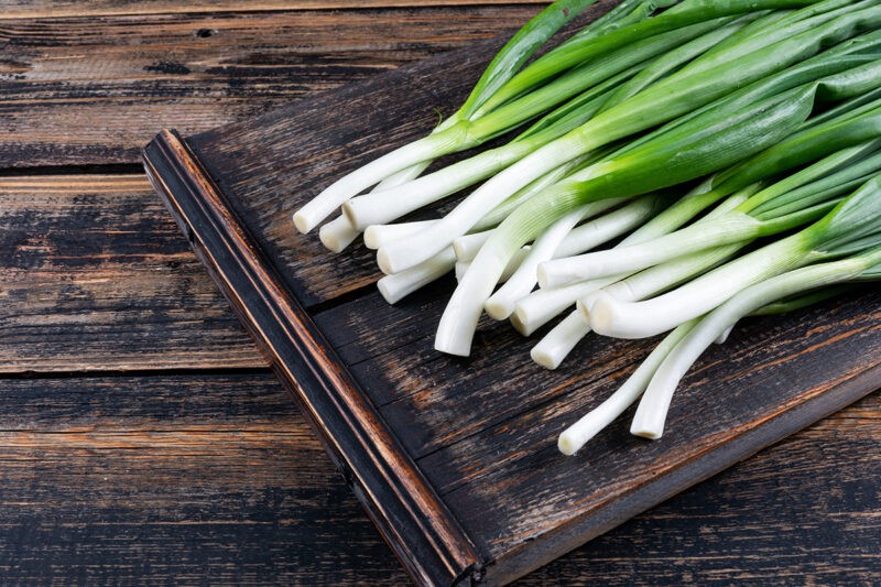Green spring onions or scallions on a cutting board on a dark wooden background. top view.