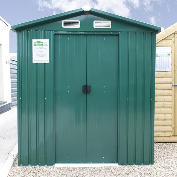 The 6ft x 8 ft Steel shed on the Sheds Direct Ireland showroom in Finglas. It's a green shed, with vertical steel sheets and white vents above the door. There is a wooden shed to the right and a block build unit to the left. The doors are closed and the black handles are visible.