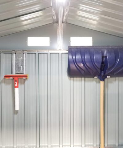 A wide angle picture of the inside of a shed with the focus on two took hooks on the back wall. One is supporting a large, blue snow shovel. The other is supporting a small, red squeegee. The hooks are 30cm long, 10cm wide and they have a picture of a shovel indented into the,