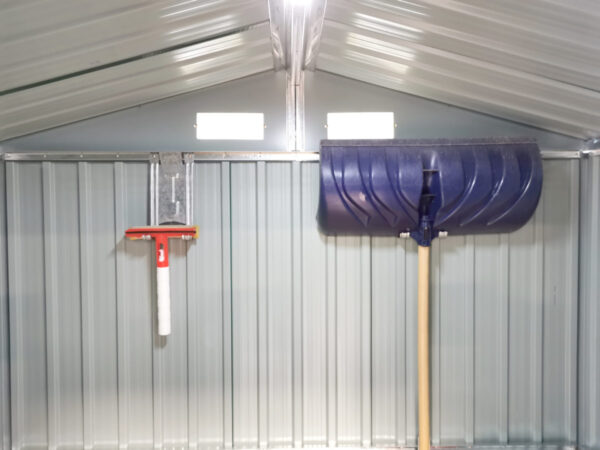 A wide angle picture of the inside of a shed with the focus on two took hooks on the back wall. One is supporting a large, blue snow shovel. The other is supporting a small, red squeegee. The hooks are 30cm long, 10cm wide and they have a picture of a shovel indented into the,