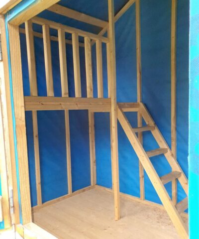 Another interior view of the wooden playhouse, it shows the blue lined walls, the wooden staircase, the hard floor and the landing.