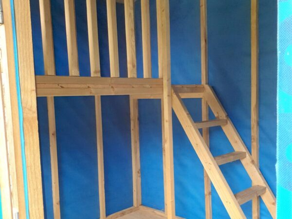 Another interior view of the wooden playhouse, it shows the blue lined walls, the wooden staircase, the hard floor and the landing.