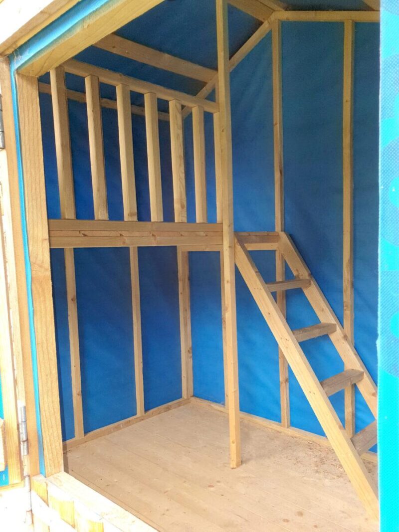 Another interior view of the wooden playhouse, it shows the blue lined walls, the wooden staircase, the hard floor and the landing.