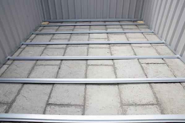 The floor frame of a PVC Cladded shed. You can see the metal bars of the frame, and the paving slabs underneath it. There is no 'floor' to speak of. Wooden plywood would suit on top of this.