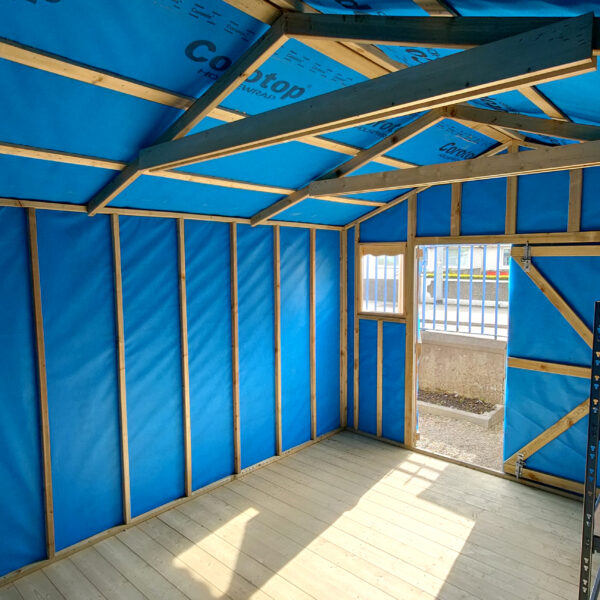 inside the taller wooden shed. The walls are a bright blue, as they are lined with membrane material and the floor is a pale wooden colour. The roof is very high up and it's reinforced with thick, darker wooden bars.