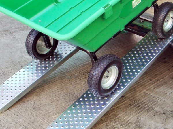 A large, empty Green bucket cart sits on two steel car ramps. The cart is at a 45 degree angle, but it is not moving. The ramps are steel, shiny and have large circular holes in them for grip. The holes are about the size of a 5c coin.