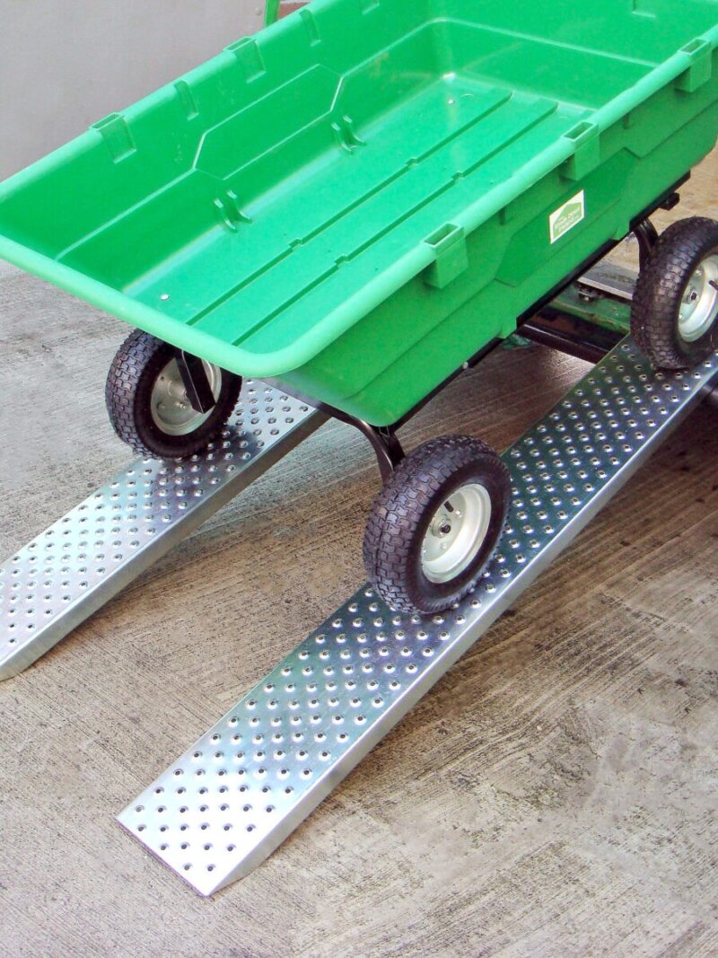 A large, empty Green bucket cart sits on two steel car ramps. The cart is at a 45 degree angle, but it is not moving. The ramps are steel, shiny and have large circular holes in them for grip. The holes are about the size of a 5c coin.