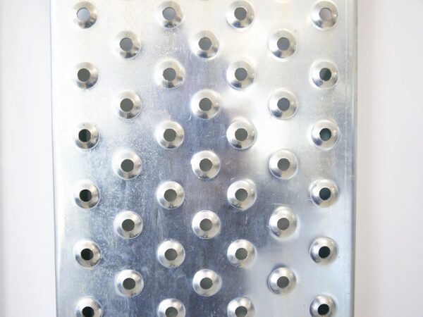 a detail, macro photograph of a car ramp. It's shiny steel with circular, bevelled holes for support.