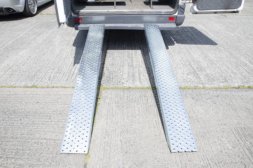 A view of the Steel Loading Ramps as seen from directly behind the bus that they are attached to. They are shiny and clean. There are extruded holes for grip. They support 1,500kg.