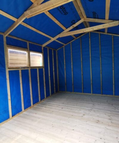Inside the taller wooden shed, showing a high apex roof. The walls are lined with a blue fabric and the supporting panels are bare. There are 2 windows to the left hand side of the shed, through which you can see another wooden shed's wall.