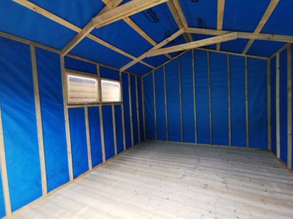 Inside the taller wooden shed, showing a high apex roof. The walls are lined with a blue fabric and the supporting panels are bare. There are 2 windows to the left hand side of the shed, through which you can see another wooden shed's wall.