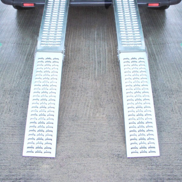 Two Folding Ramps lined up and raised to the back of a green van. The ground below is slick and wet looking and it reflects