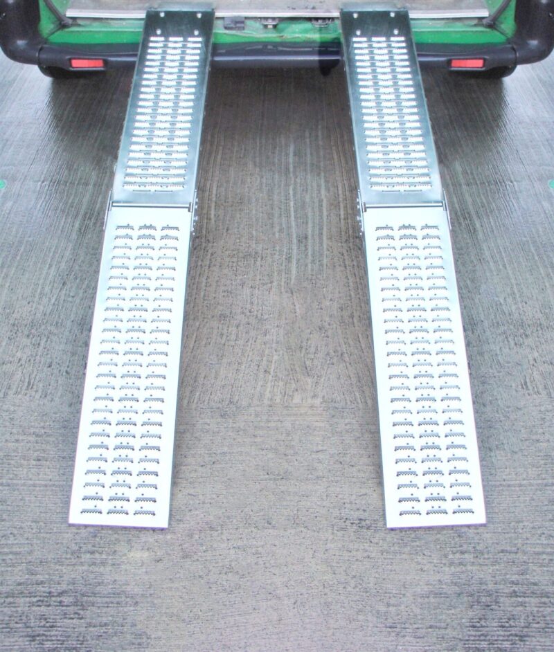 Two Folding Ramps lined up and raised to the back of a green van. The ground below is slick and wet looking and it reflects