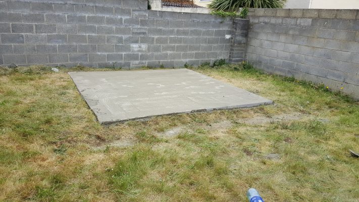 A solid, level concrete base with grass around it. The base is raised and it's perfect to put a shed on.