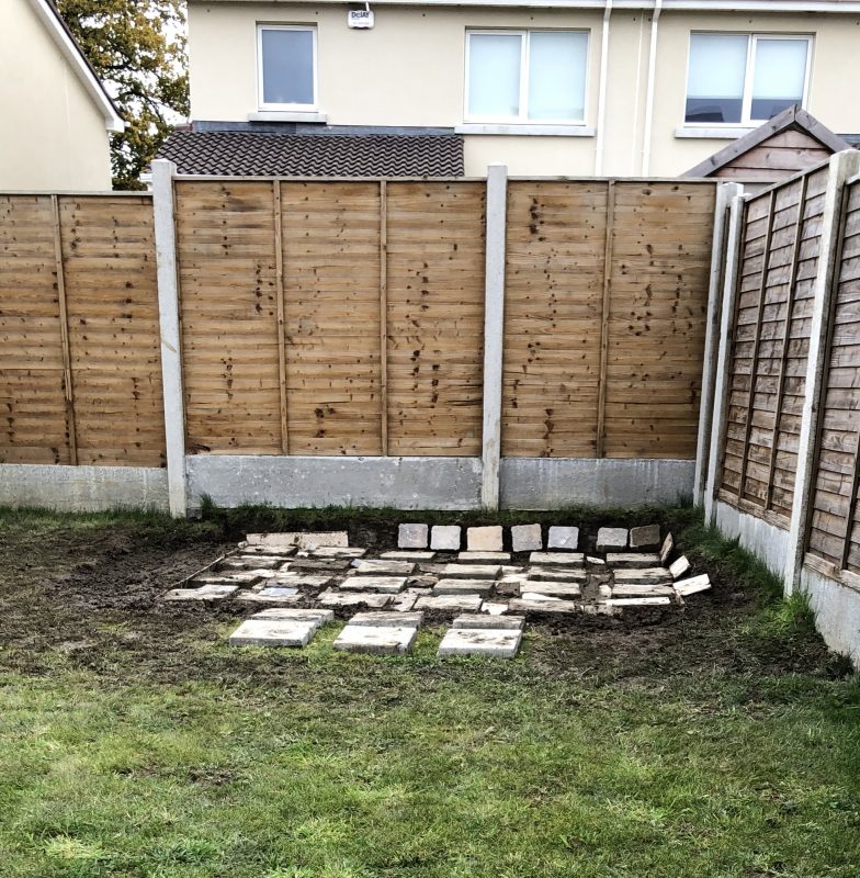 Paving Slabs laid out on a sloped batch of grass. The paving slabs are not connected together, they are both raised above and sunk into the grass and some are at an almost 45 degree angle on the bank of the back wall of the garden.