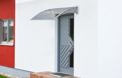 A Door canopy above a grey, heavy steel looking door. The walls are white and red. The house looks moder. The canopy, arches over the doorway. 